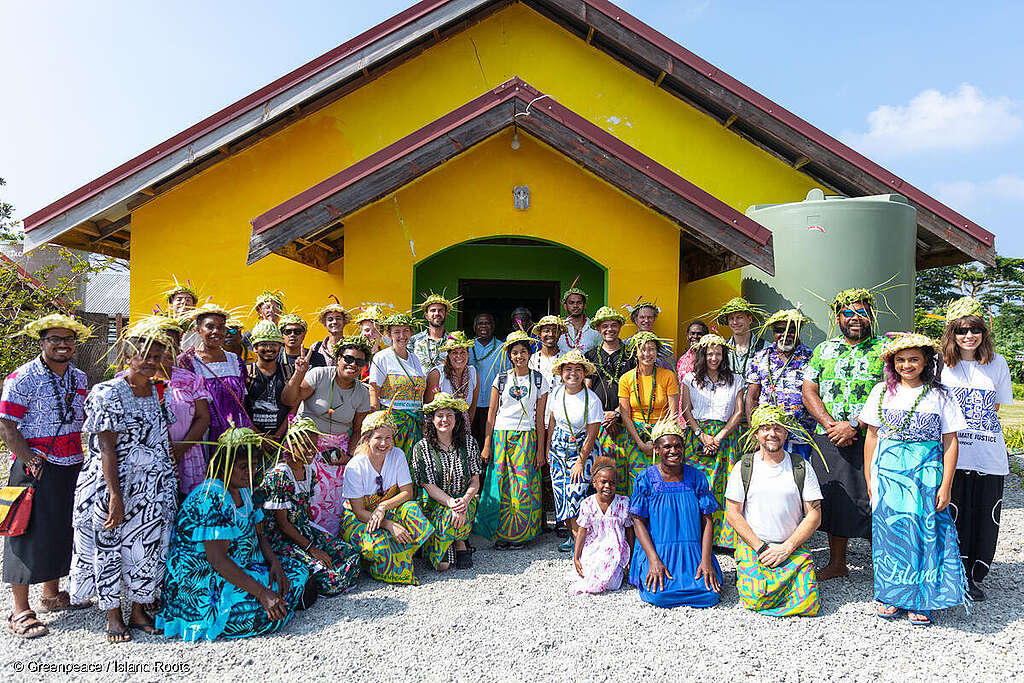 Greenpeace staff and ni-Vanuatu community members stand outside a bright yellow church building. 